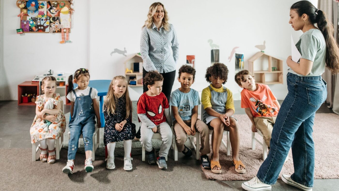 Group of diverse children in a kindergarten classroom attending an interactive learning session with teachers.