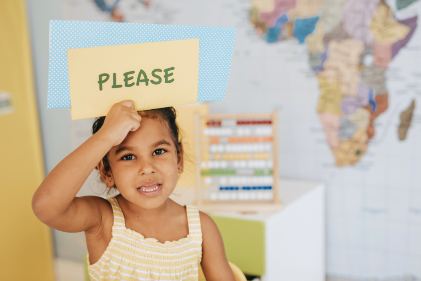 A young girl holding a please sign